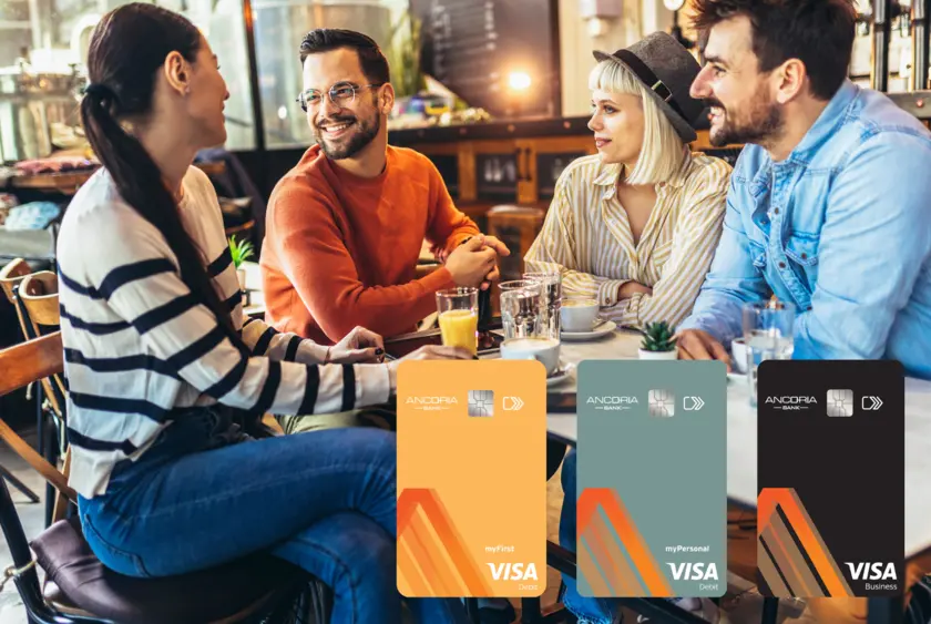 A group of people sitting and talking. On the bottom right side there are the three Ancoria Bank Visa debit cards for students, individuals and businesses.