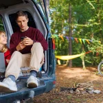 A couple siting in a car in nature using mobile banking and online banking.